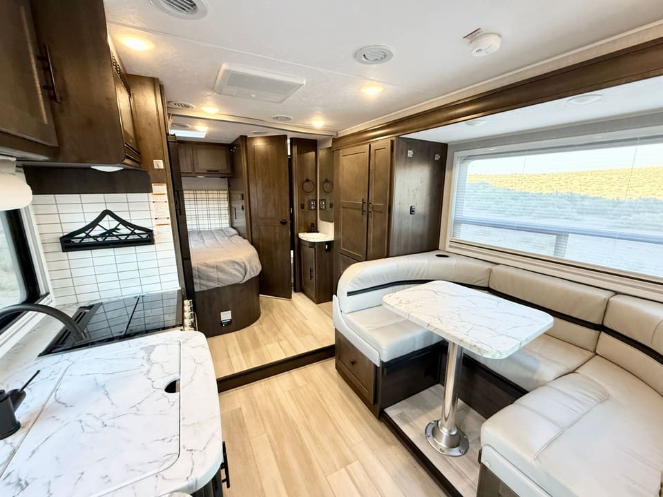 Living area with U-shaped leather dinette in the slide-out, rear bed and bathroom behind